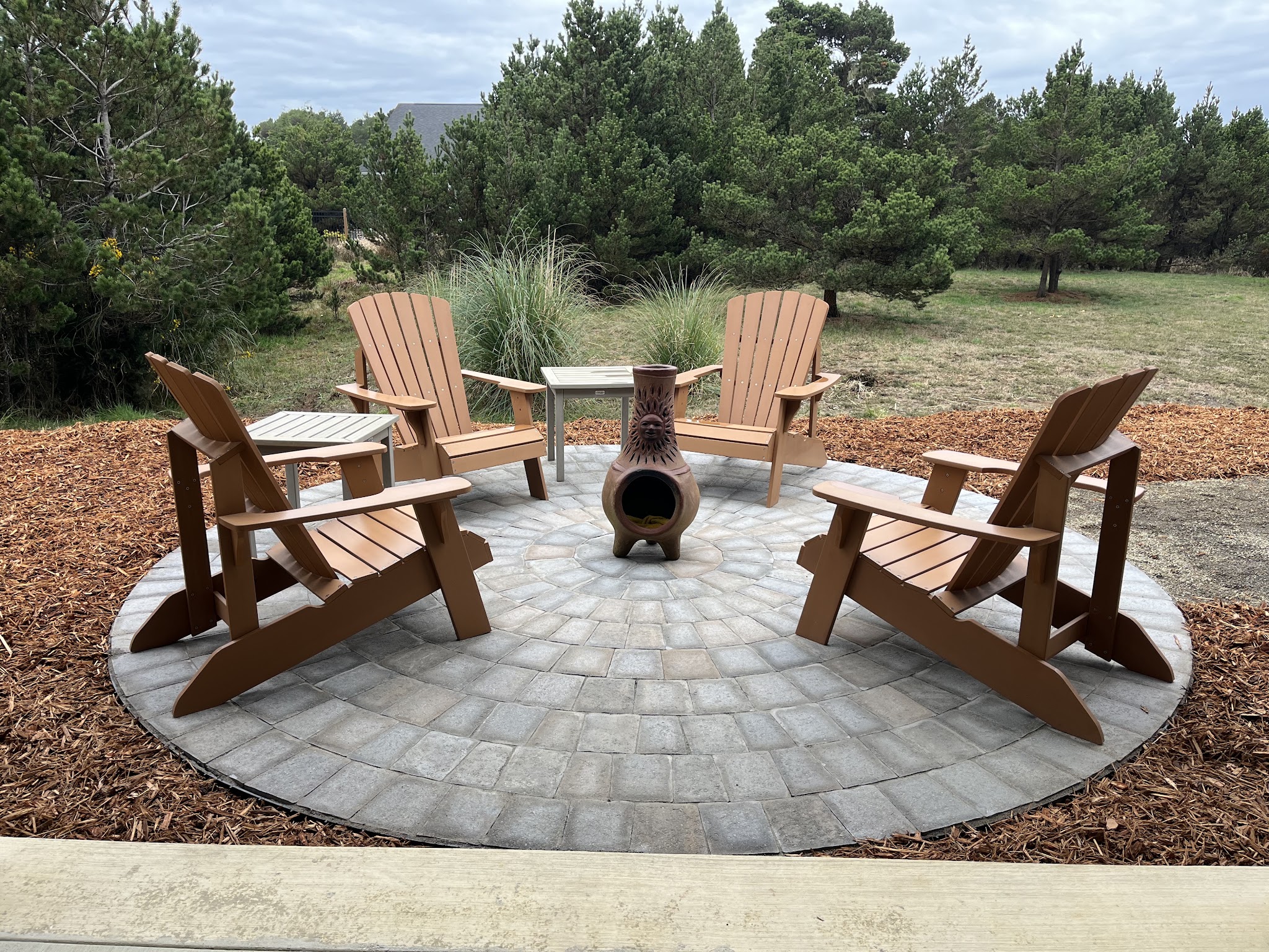 Finished outdoor living space with a circular paver patio, Adirondack chairs and a ceramic chiminea fire feature