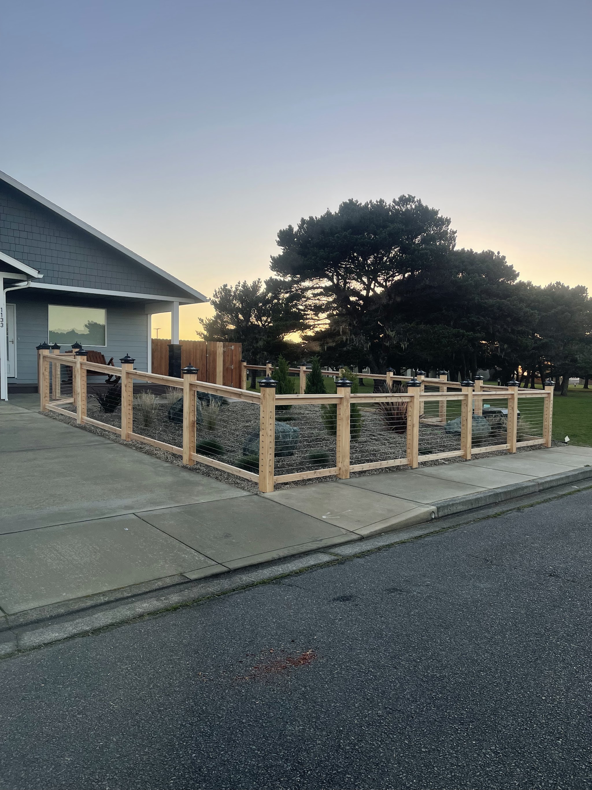 New cedar-post fence enclosing a front-yard gravel and xeriscape bed in front of a Bandon, Oregon home