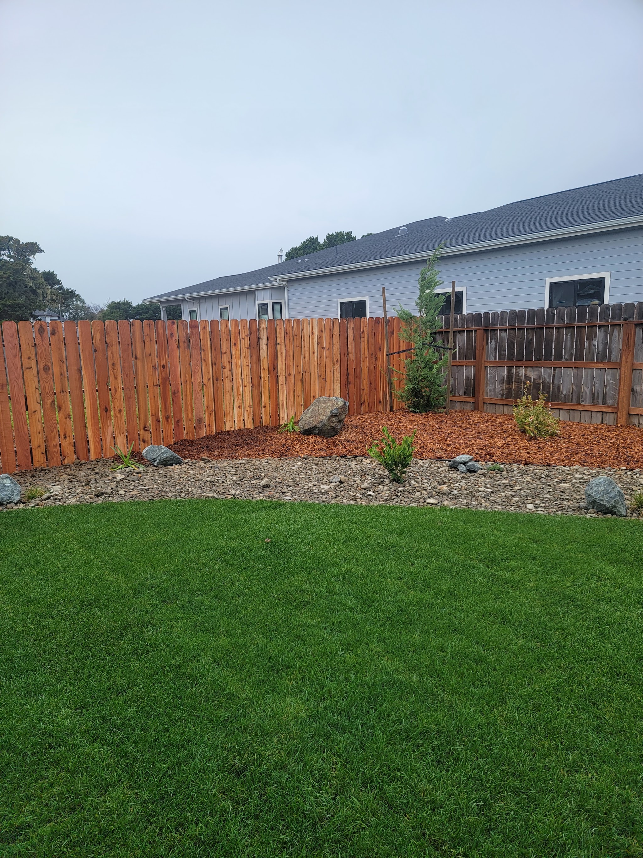 Finished backyard hardscape with a rock border, mulched planting bed, boulders and fresh sod against a cedar privacy fence