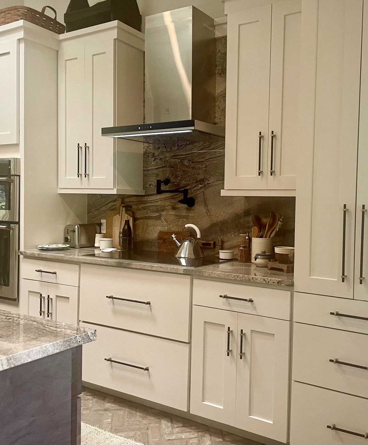 Kitchen remodel detail showing a stainless range hood, stone slab backsplash and pot-filler faucet